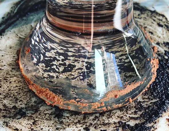 A glass jar resting in a bed of ground cocoa husks, used to grind pigment for cocoa ink.